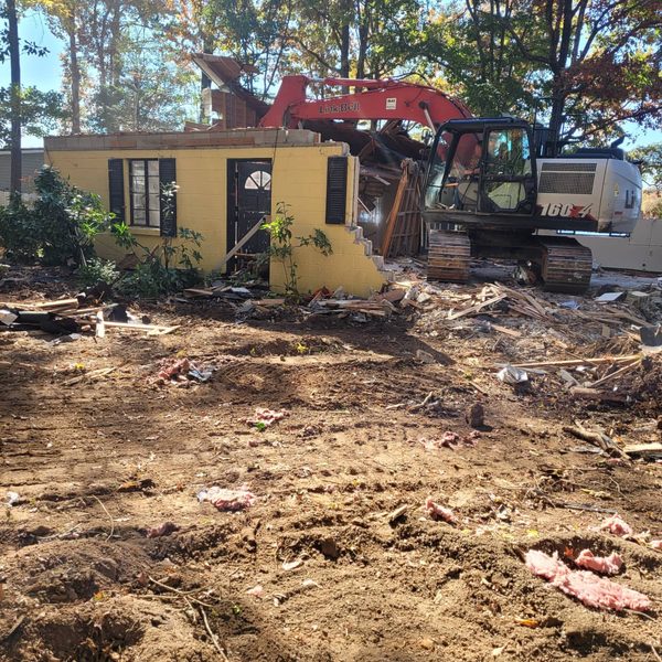 Excavator tearing into the roof of a yellow stucco building