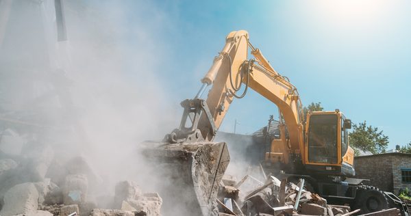 Excavator working in a cloud of dust demolishing a masonry wall