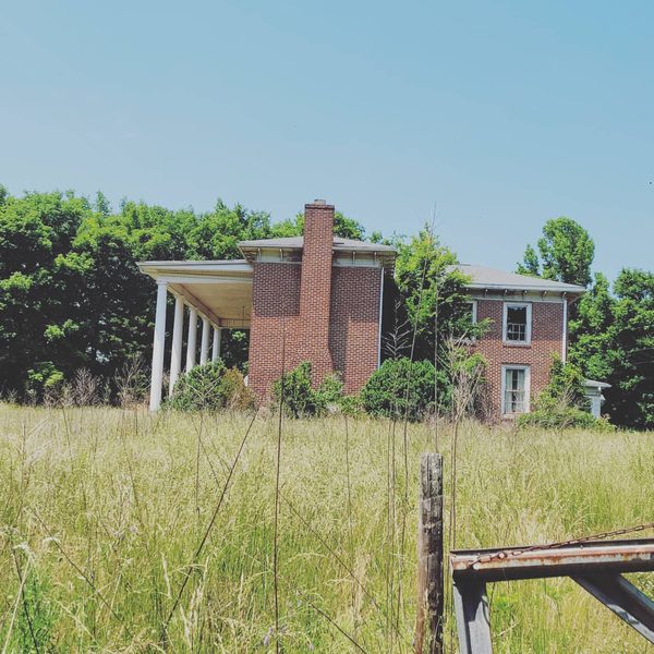 Vacant brick house with columns, overgrown and awaiting demolition