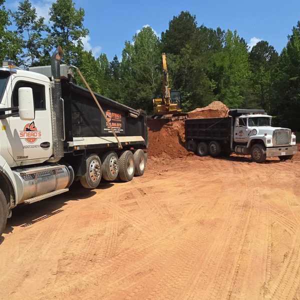 Excavator loading two dump trucks with red fill dirt