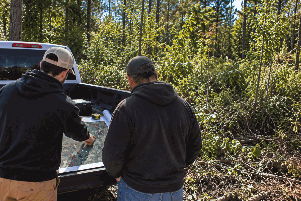 Two crew members going over a property map on a pickup tailgate beside thick brush
